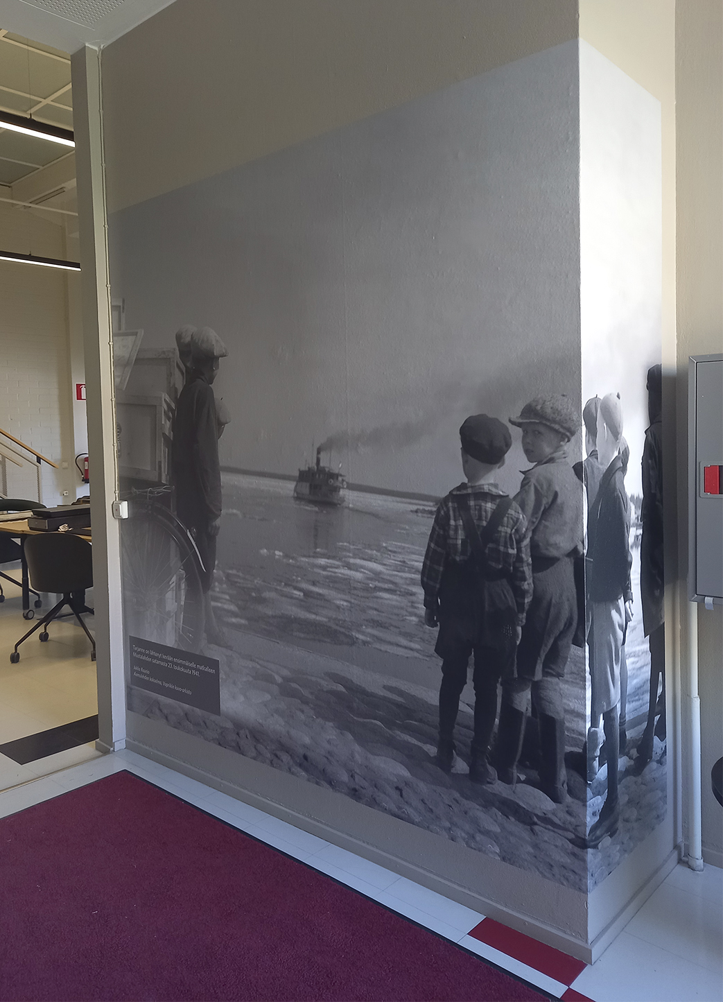 Esimerkkikuva kuvasuurennoksesta. Kuva-arkiston käytävän seinälle on laitettu tuloste lapsista ja Tarjanne -höyrylaivasta