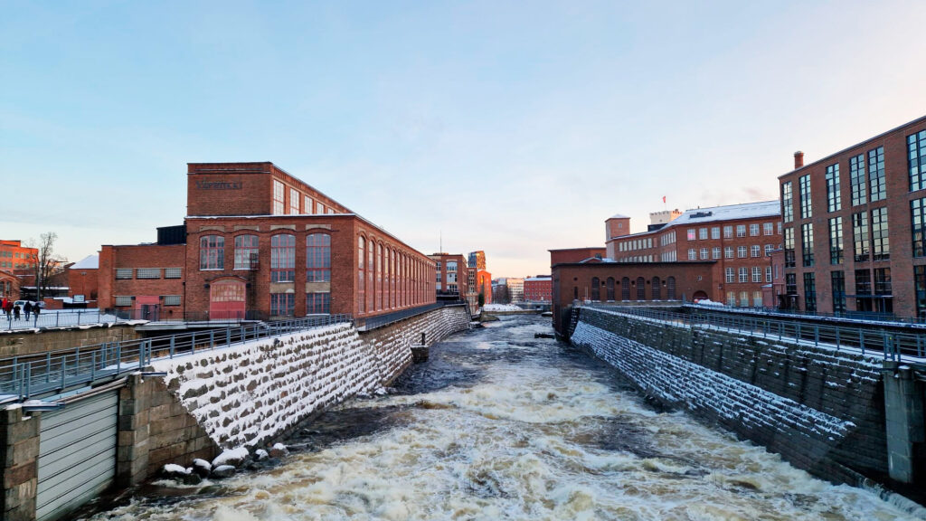 Kuohuavaa koskimaisemaa sillalta kuvattuna. Taustalla Tampereen kaupunki,e dessä museokeskus Vapriikki.